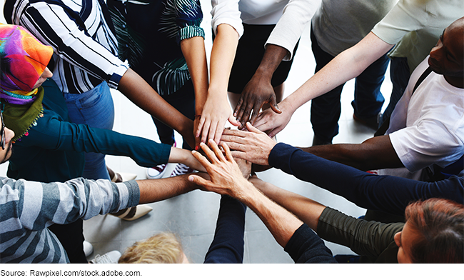 Diverse group of people in a circle putting their hands together.