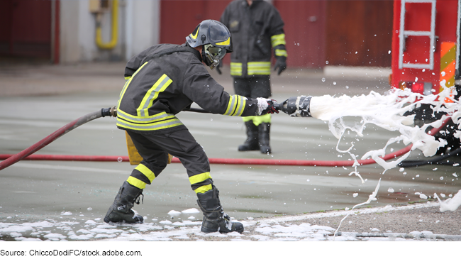 A firefighter holding a hose spraying white foam.