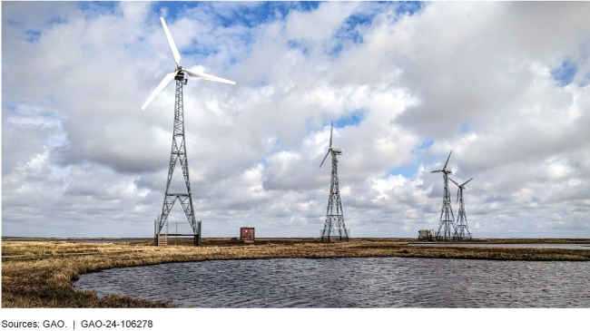 Four wind turbines near a small body of water.