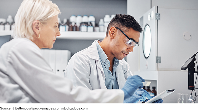 Two people in white lab coats and gloves in a laboratory. 