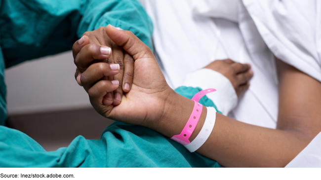 Medical personnel holding the hand of a patient wearing medical wristbands and lying in bed.
