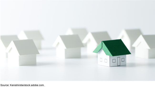 Simple white miniature houses with one single house with a green roof in the foreground