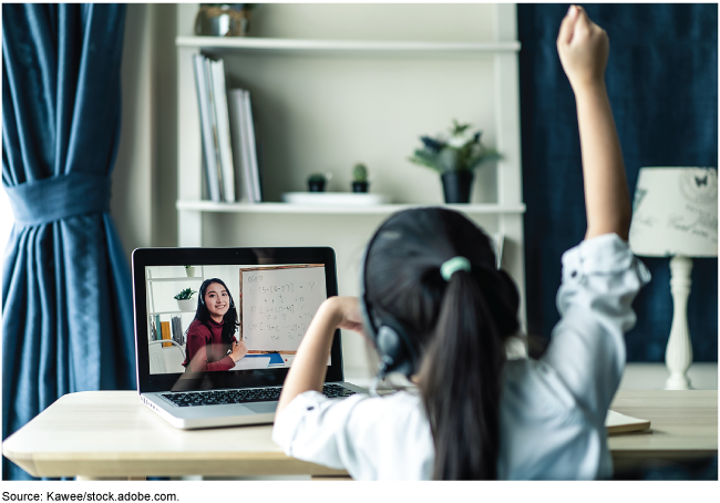 A girl with headphones on raises her hand while participating in an online program.