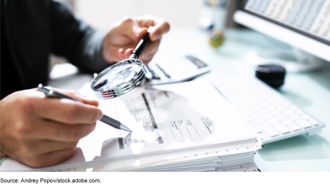 Person looking at a paper through a magnifying glass