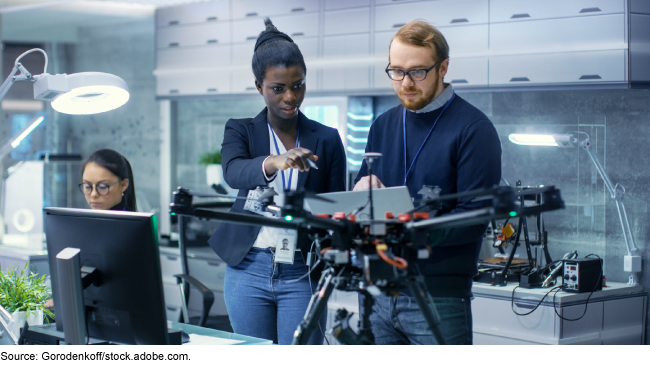 Three people working in an office while a drone floats in front of them.