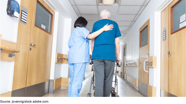 A senior citizen who uses a walker next to a medical staff member in a hallway.