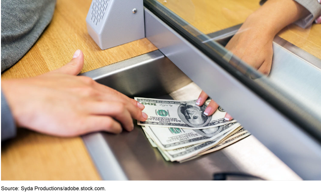 Money being passed to a person under a transparent barrier.