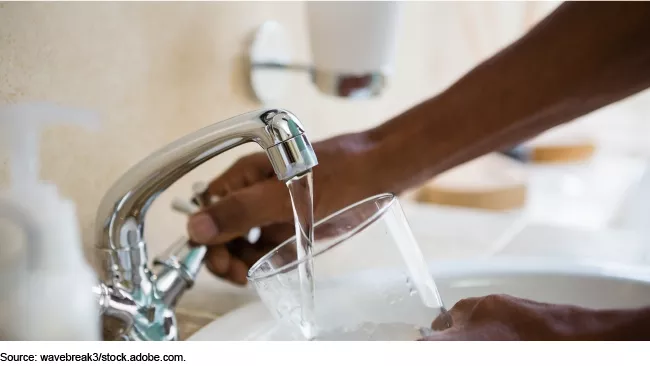 Photo showing someone filling a drinking glass with water from a kitchen faucet.