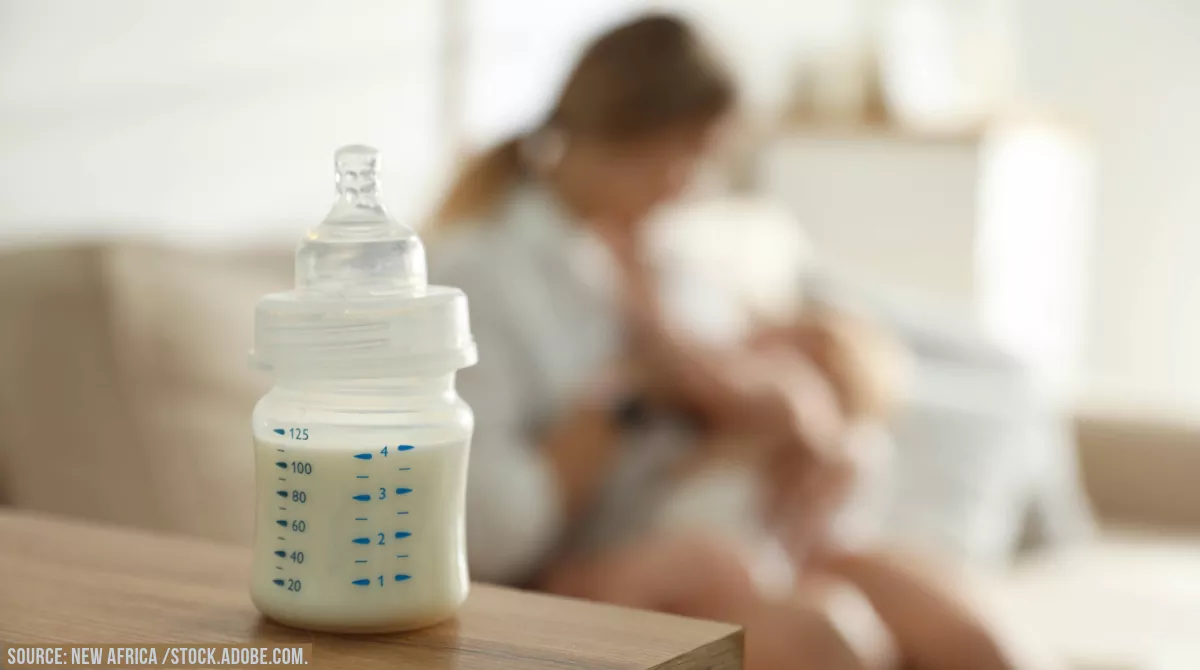 Stock image showing a baby bottle in the foreground and a parent and baby in background