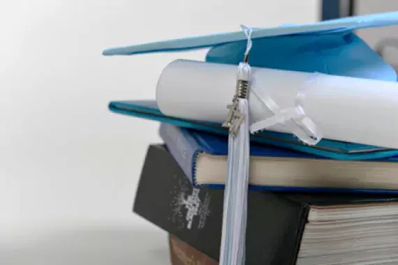 Photo of books, diploma and graduate cap.