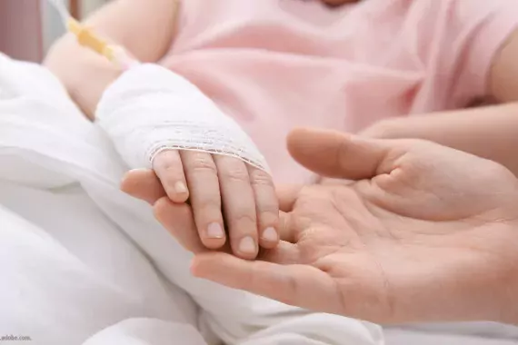 Photo showing a child with an IV in her arm holding hands with an adult, maybe a parent or medical worker