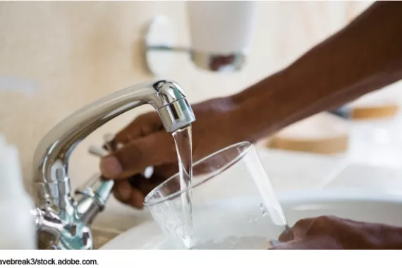 Photo showing someone filling a drinking glass with water from a kitchen faucet.