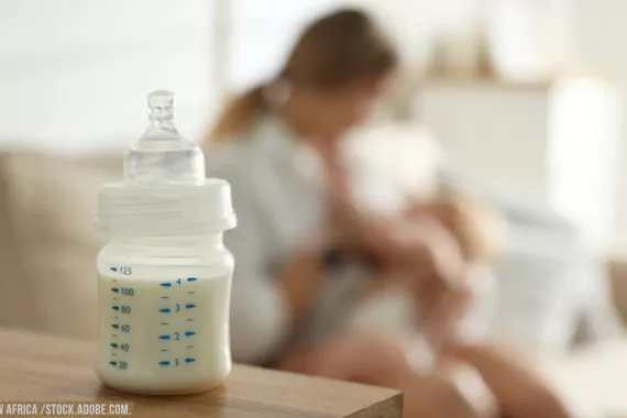 Stock image showing a baby bottle in the foreground and a parent and baby in background